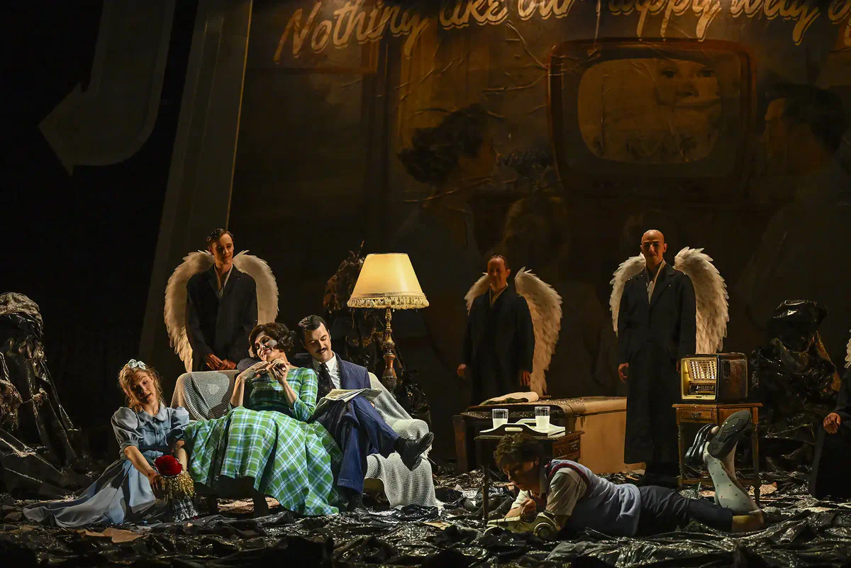 Escena de Hansel y Gretel con varios intérpretes reunidos en un salón y figuras con alas al fondo.