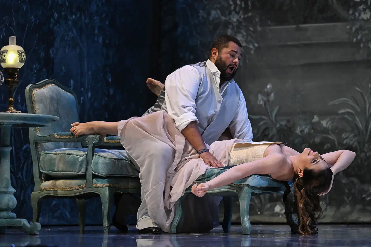 Escena de Manon con un hombre inclinado sobre una mujer recostada entre dos sofás.