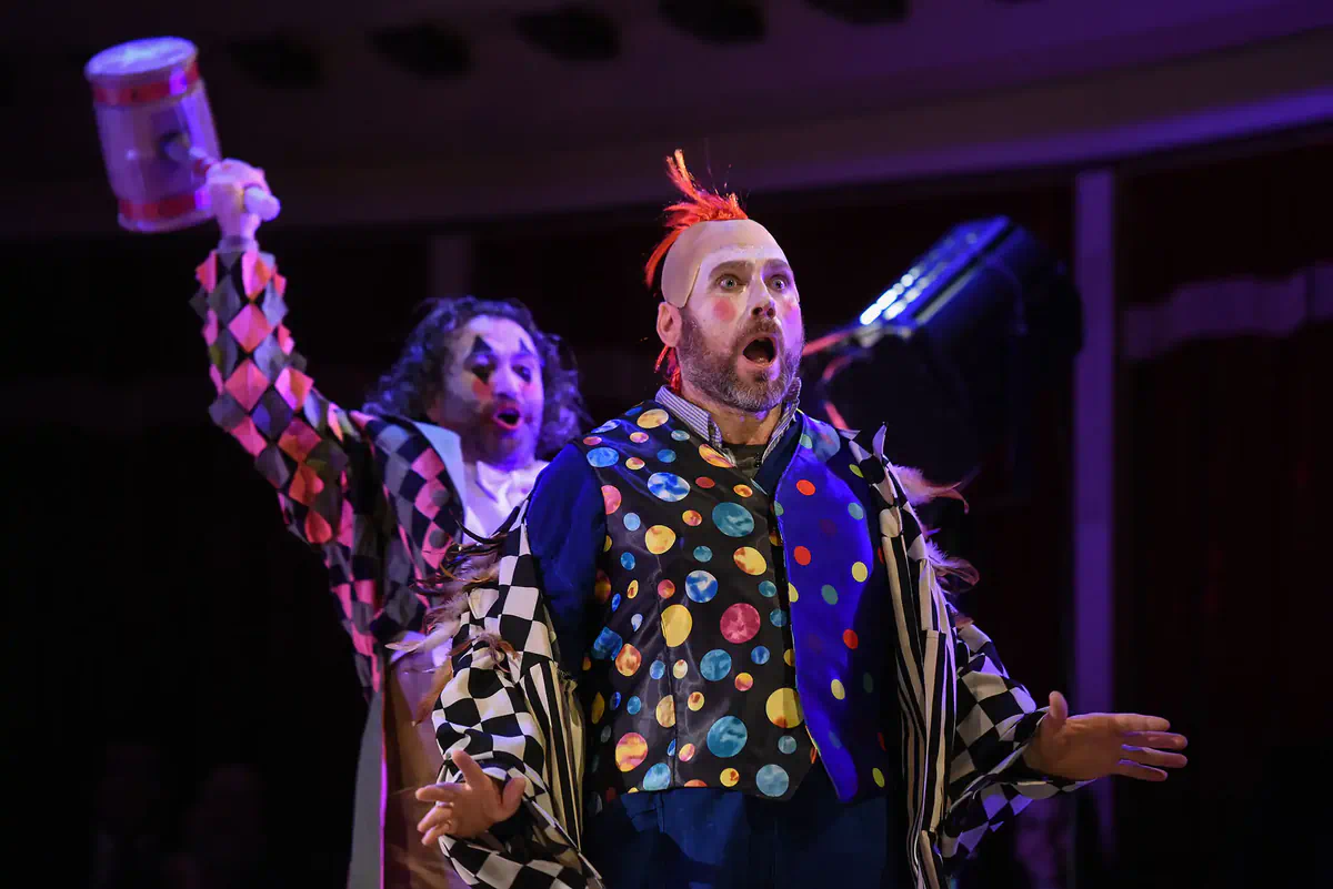 Escena de Pagliacci con un intérprete de traje de lunares y tocado rojo en primer plano.